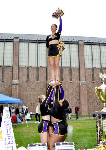 A cheerleader waves a pom pom in the air while being lifted high by her bases and backspot
