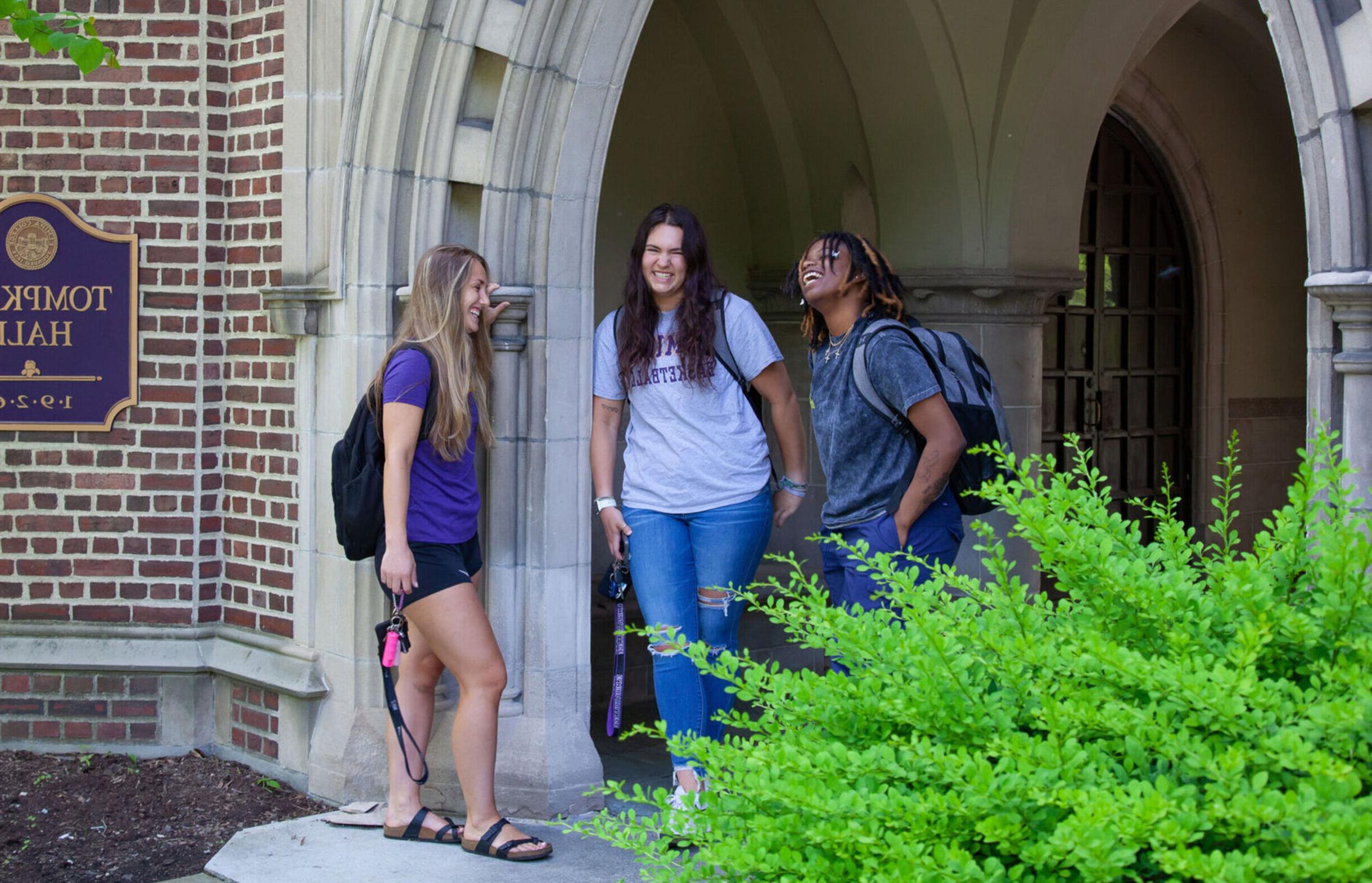 Three female students laugh while hanging out at the entrance of Tompkins Hall
